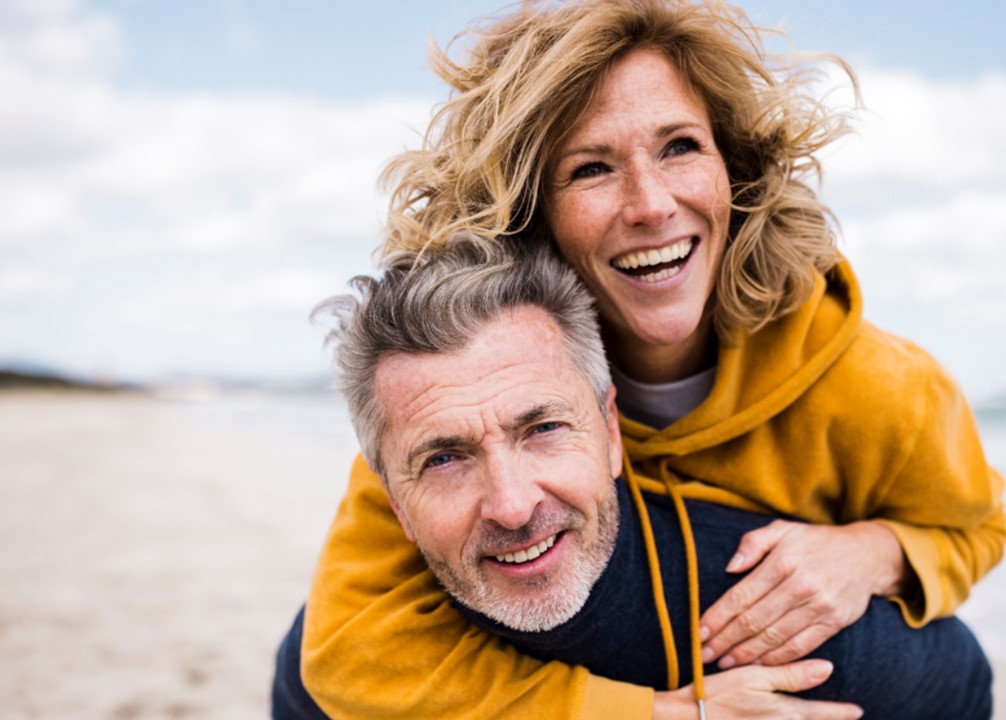 Anne and Paul smiling in embrace on a beach